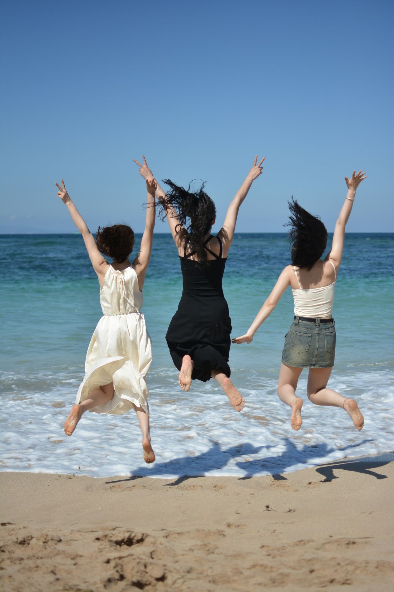 Three women joyfully jump on a sunny beach.